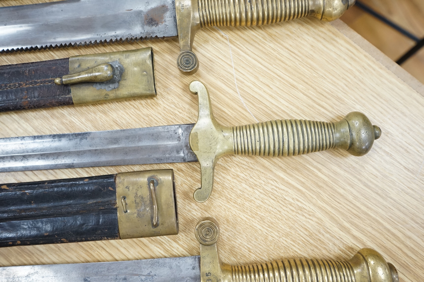 Three Continental infantry officer’s sidearms briquette, the first stamped Paris, in its brass mounted leather scabbard, another similar with sawback blade (illegible stamp), and another similar with thin blade, stamped
